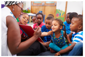 woman in front of group of children reading a book