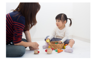 mom and daughter sitting on floor together playing with basket of toys