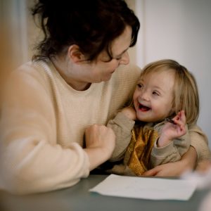Smiling mother playing with disabled daughter while sitting by table at home