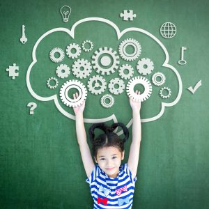 Young girl in front of a chalkboard. A cloud is drawn with gears inside and key and puzzle icons surrounding it