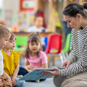 three children listen and watch as their teacher reads a book